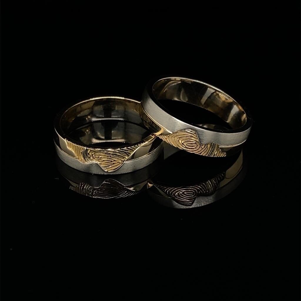 Twee trouwringen van zilver en goud, afgebeeld op een zwart reflecterend oppervlak.