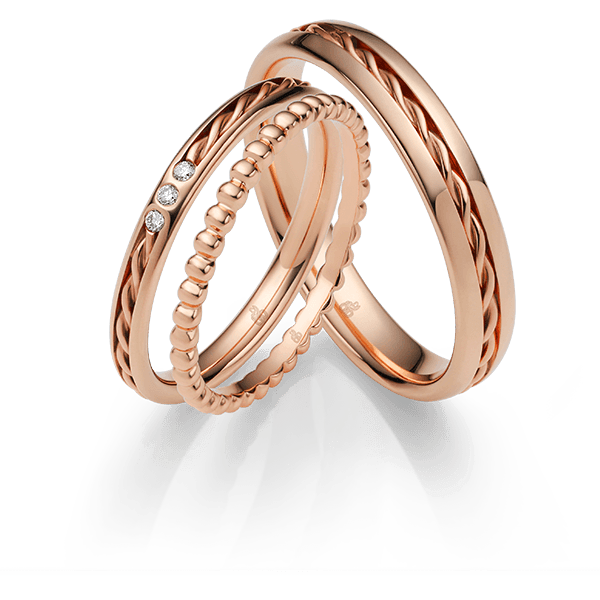 Trouwringen van roségoud; één met drie diamanten, een andere met een gevlochten ontwerp en de derde met kleine kraaltjes.