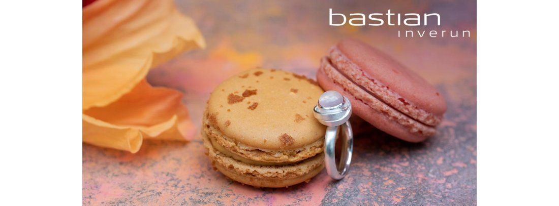 Een zilveren ring met een edelsteen naast macarons, op een kleurrijke achtergrond.