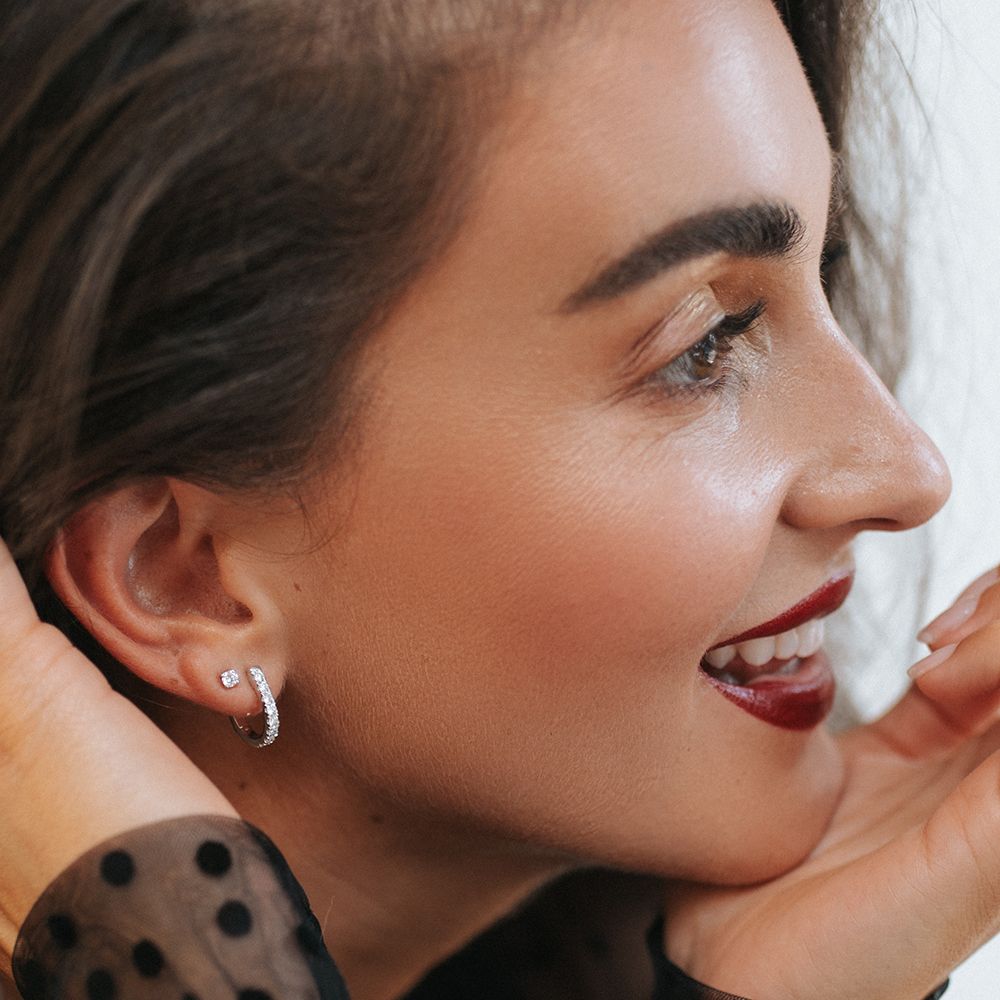 Vrouw met donker haar, oorringen en stekers, glimlachend en met donkere lippenstift.