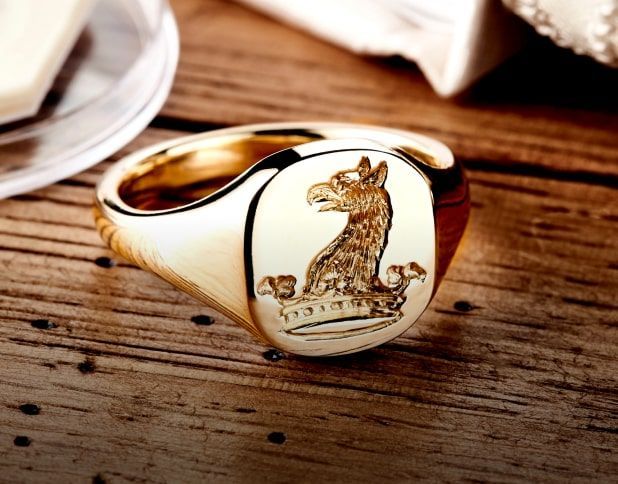 Gouden zegelring met een gesneden griffioenwapen op een houten oppervlak.