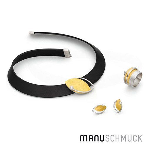 Sieradenset: zwarte ketting met ovale hanger van goud, oorbellen en een ring; witte achtergrond.