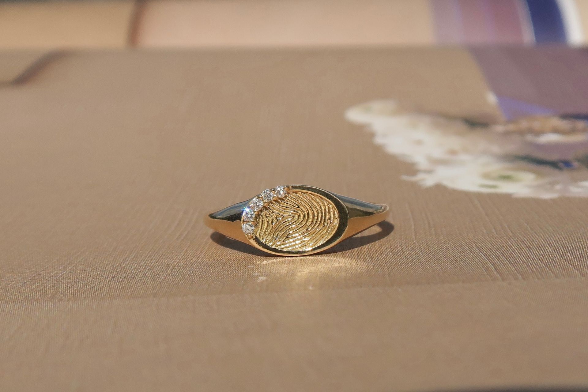 Gouden ring met vingerafdrukontwerp en kleine diamantjes op een gestructureerd oppervlak.