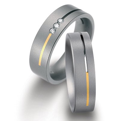 Twee trouwringen: grijze metalen banden met gouden en diamanten accenten.