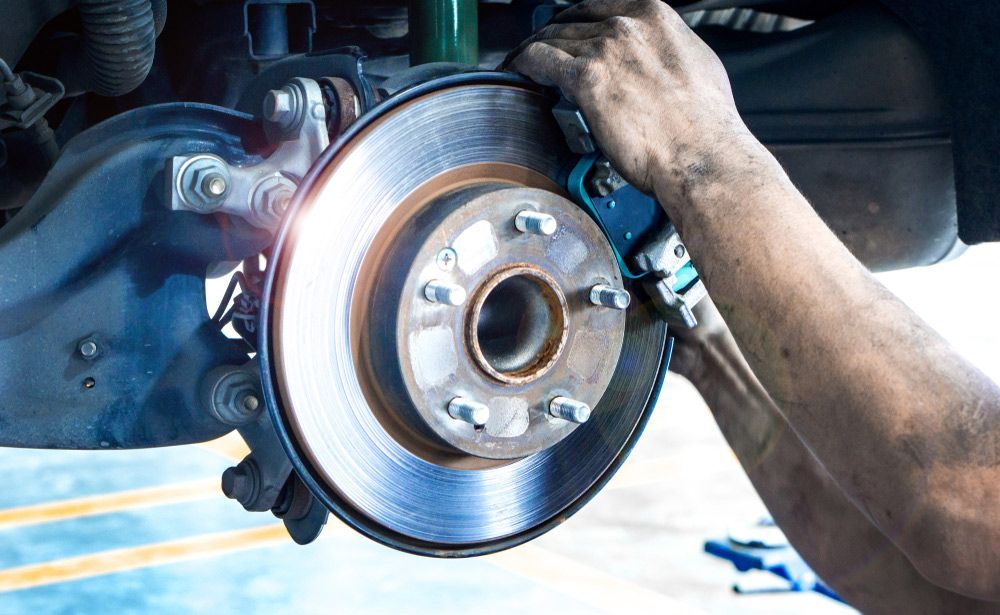 A Man Is Fixing a Brake Disc on A Car with A Wrench — Currajong Brake Parts Pty Ltd In Currajong, QLD