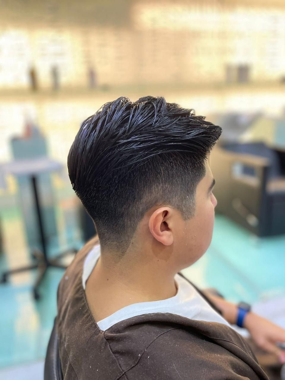 Perfil de una persona con un corte de pelo corto degradado sentada en una silla de barbería, con el salón desenfoque de fondo.