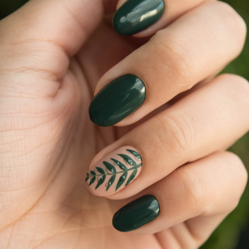 Mano con uñas de color verde oscuro y una uña decorada con un diseño de hojas.
