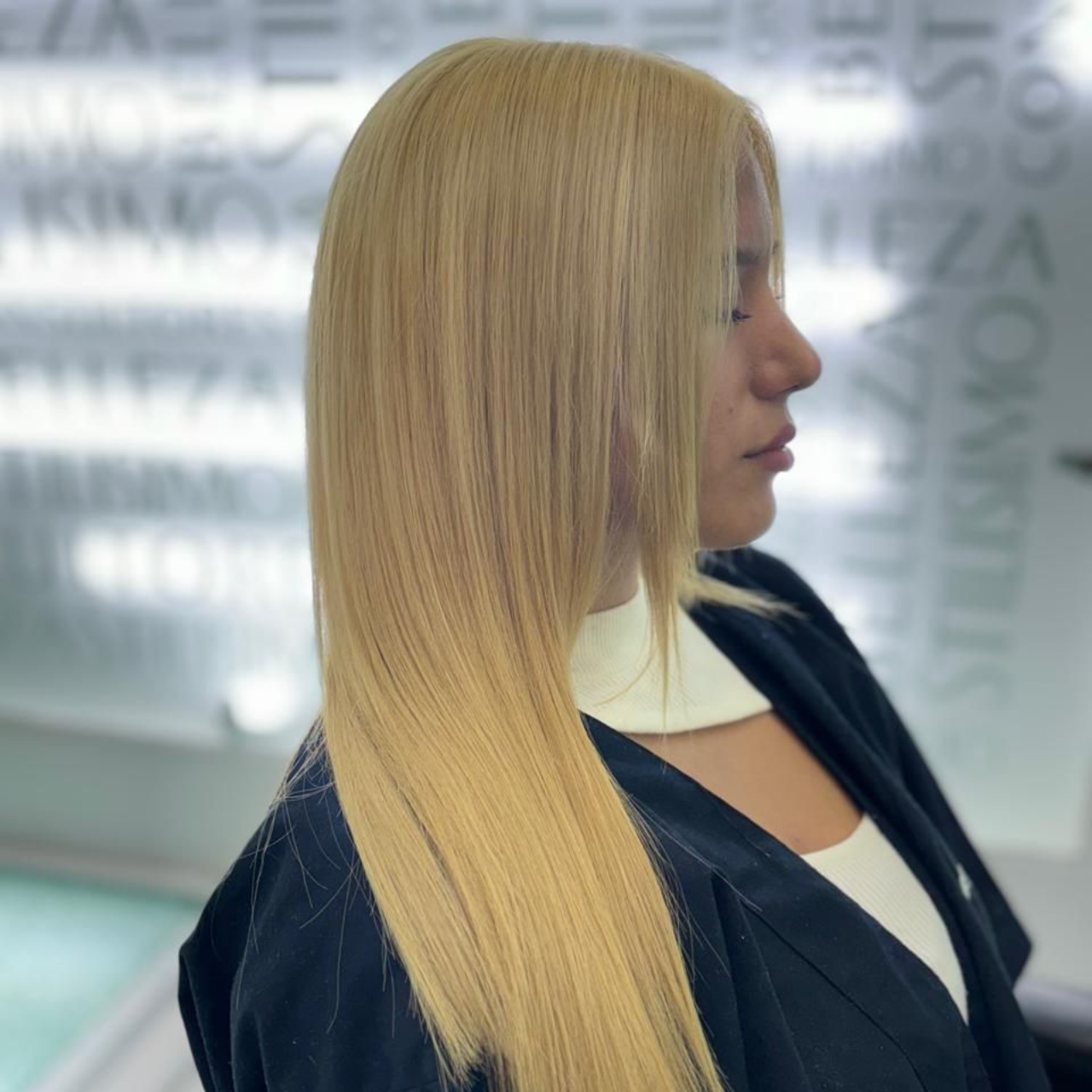 Perfil de una mujer rubia con un blazer oscuro de pie en un entorno de oficina moderno.