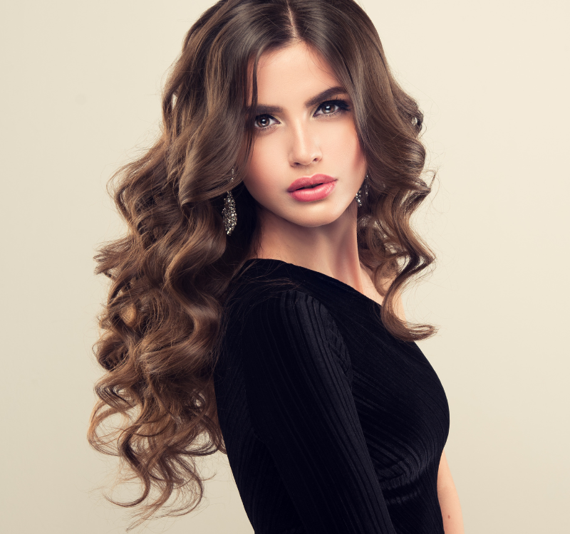 Retrato de una mujer con cabello castaño largo y ondulado, vestida con un vestido negro sobre un fondo beige.