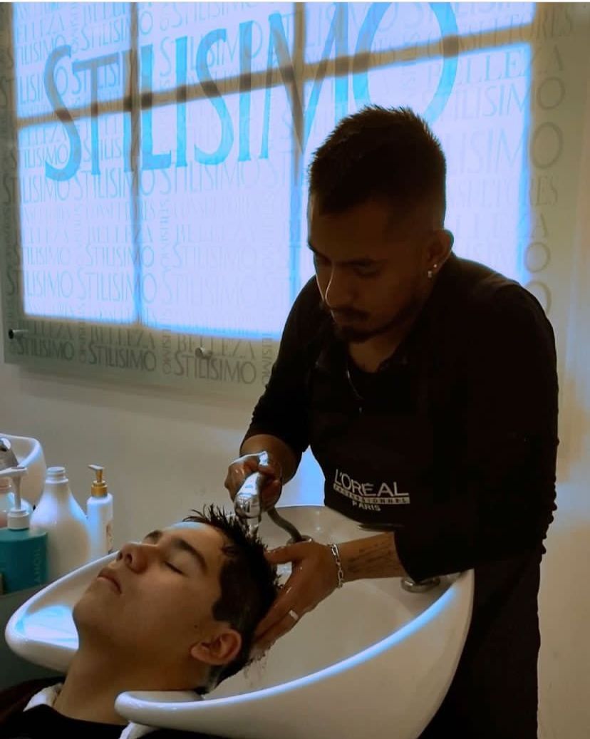 Una peluquera lava el cabello de una clienta en el lavabo de un salón de belleza, con botellas de champú cerca.