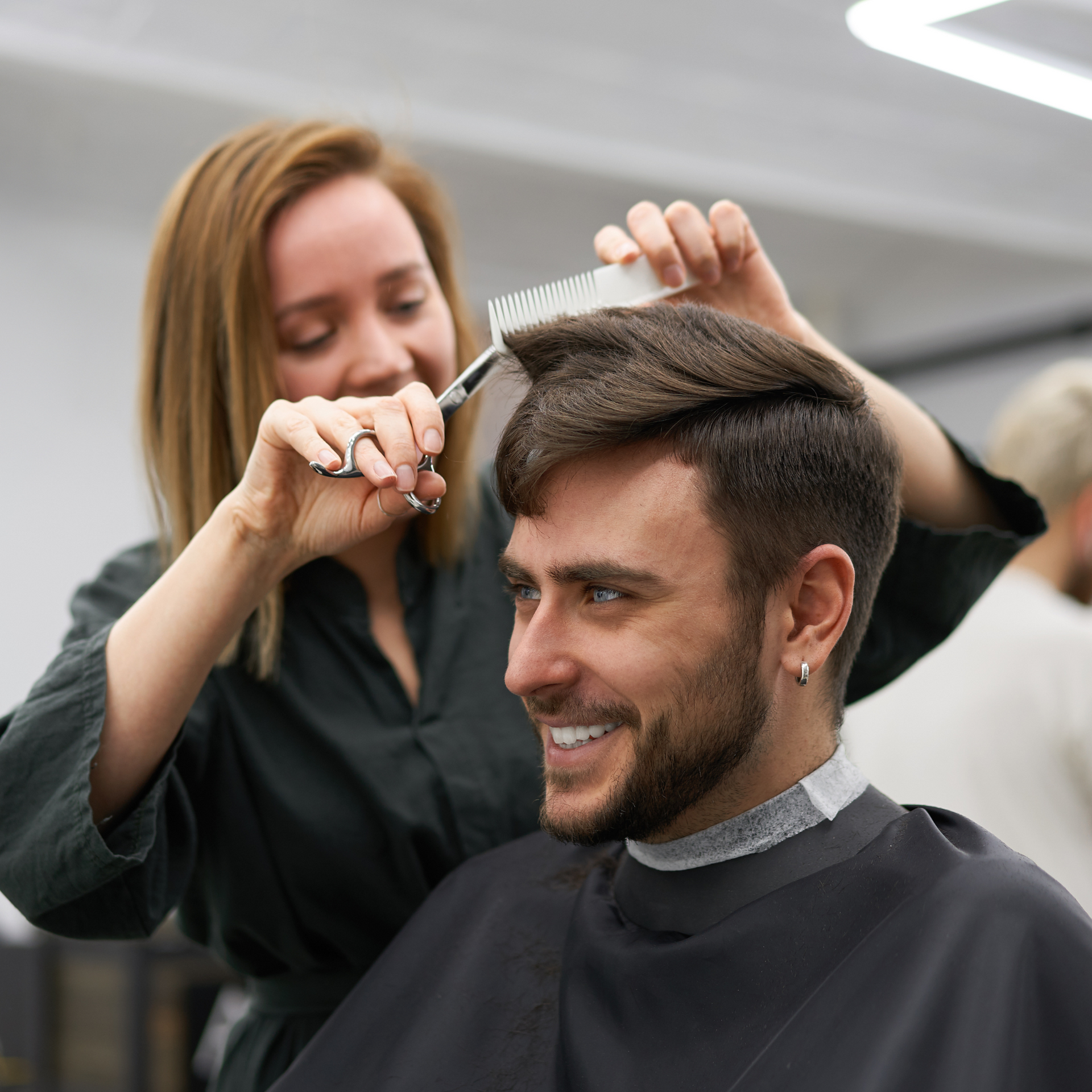 Una peluquera le corta el pelo a una clienta sonriente en un salón de belleza.
