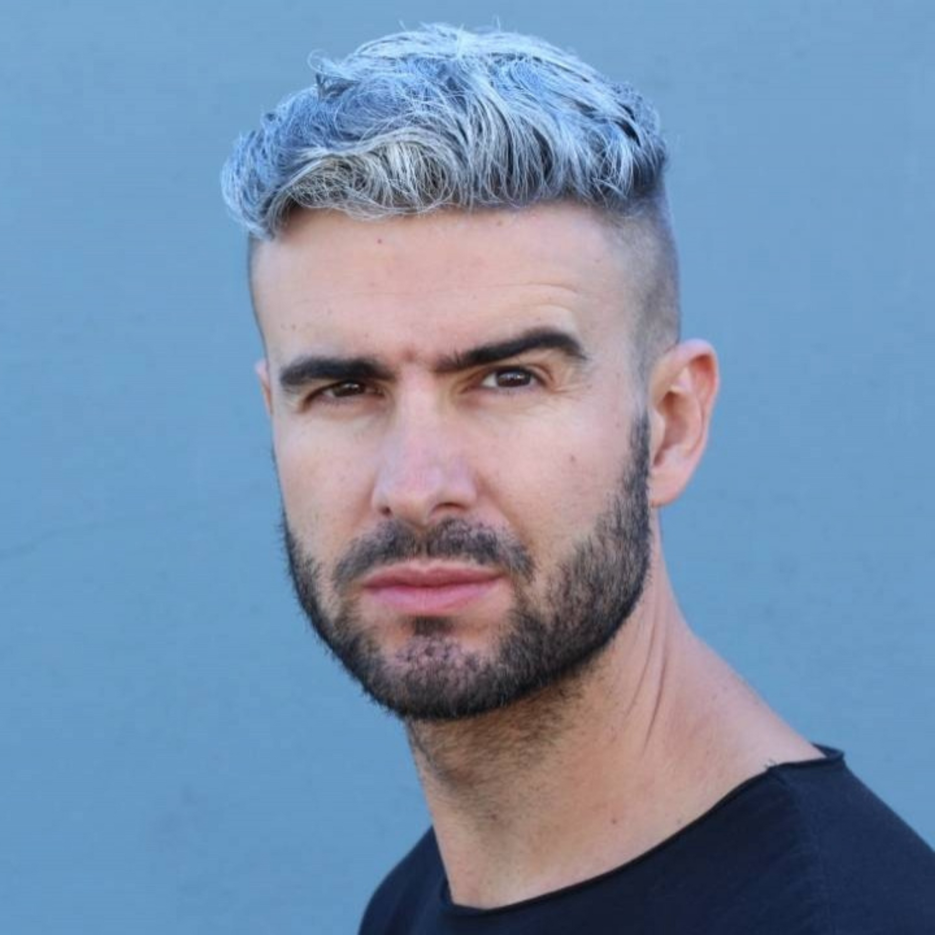 Retrato de un hombre con cabello plateado y barba corta sobre un fondo azul.