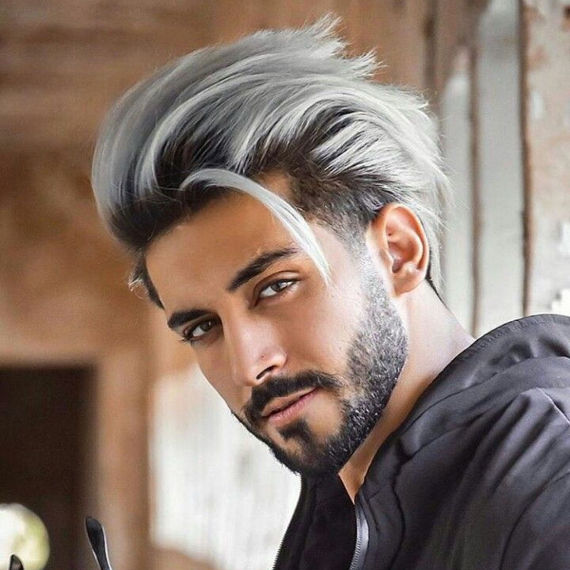 Retrato de un hombre con cabello y barba con mechones plateados, que viste una chaqueta oscura, sobre un fondo interior desenfocado.