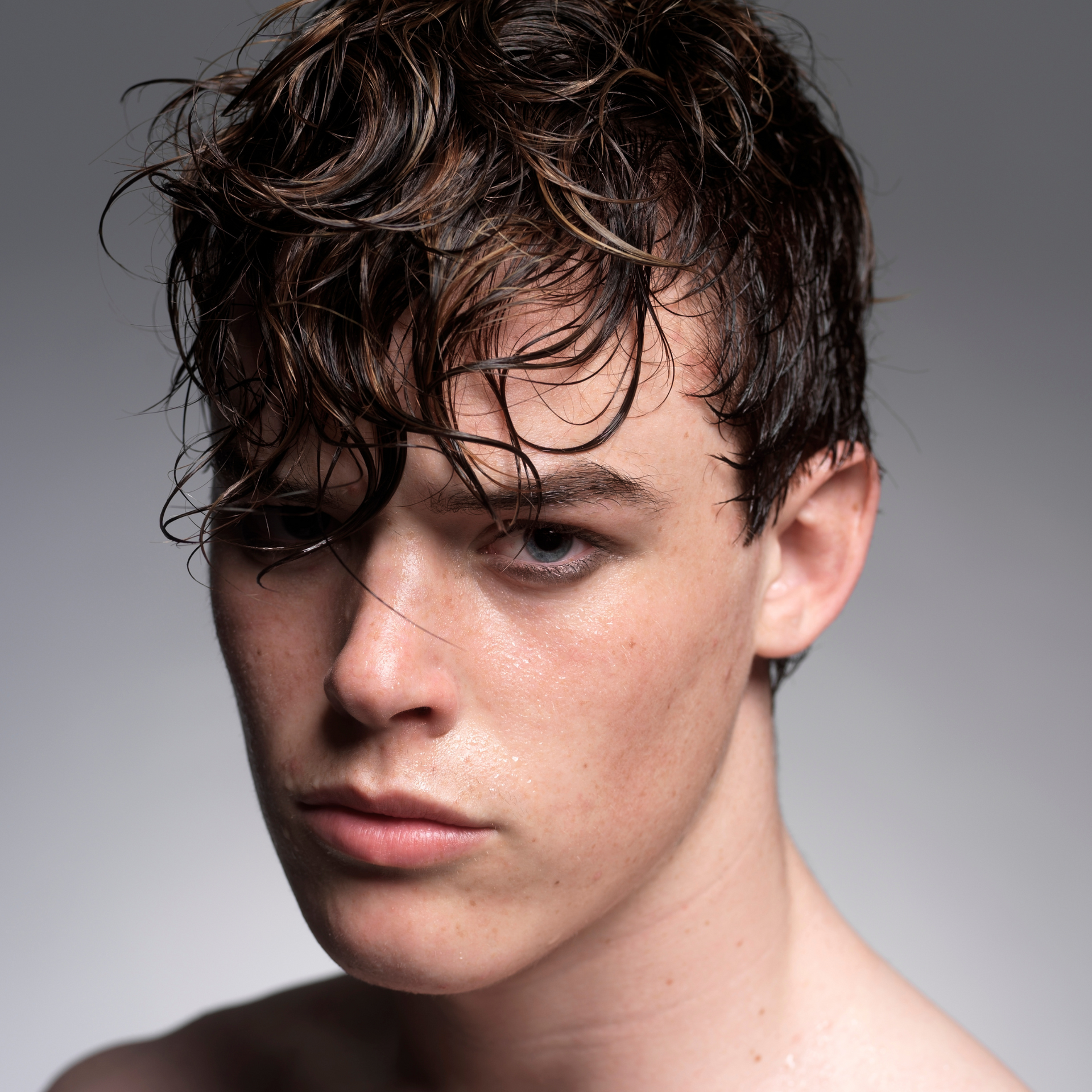 Retrato de una persona con cabello rizado y mojado sobre un fondo gris liso.