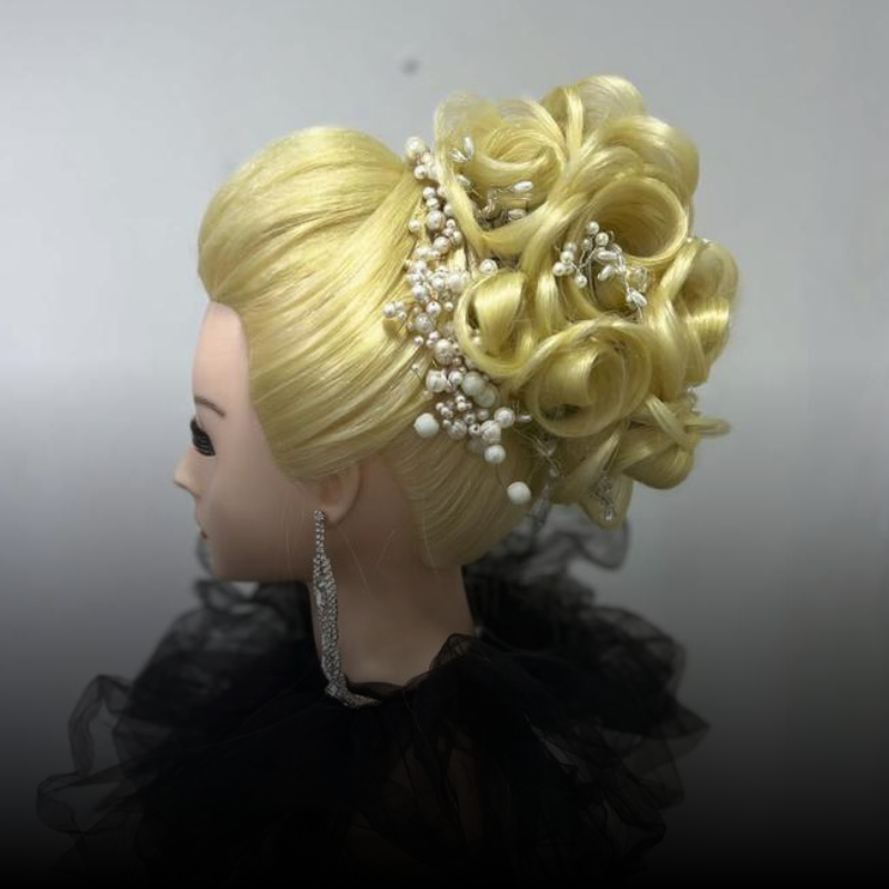 Cabeza de maniquí rubia con un elegante recogido rizado, detalles de perlas y cuello negro con volantes sobre un fondo gris.