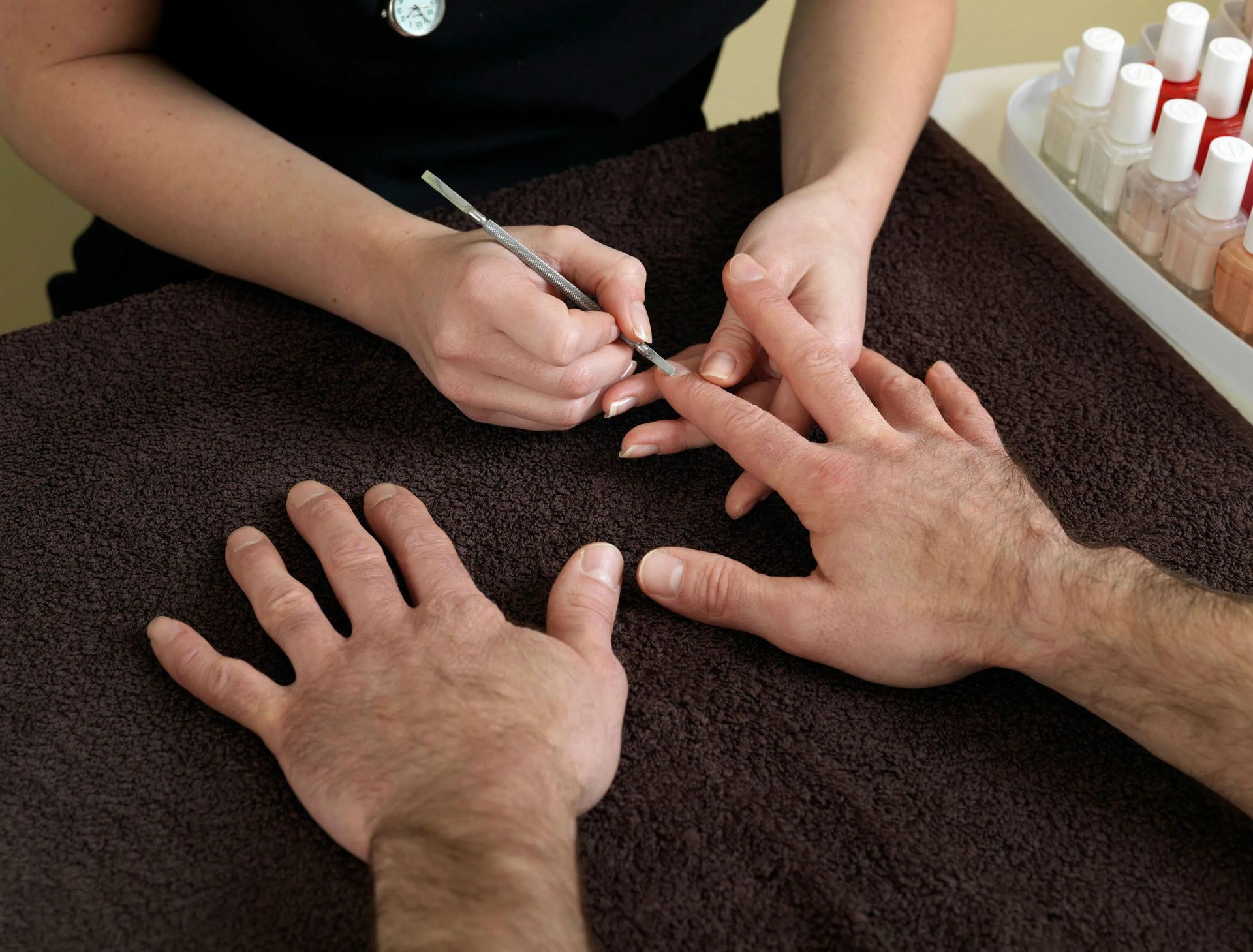 Manicura en proceso: manos sobre una toalla mientras una técnica de uñas pinta las uñas.