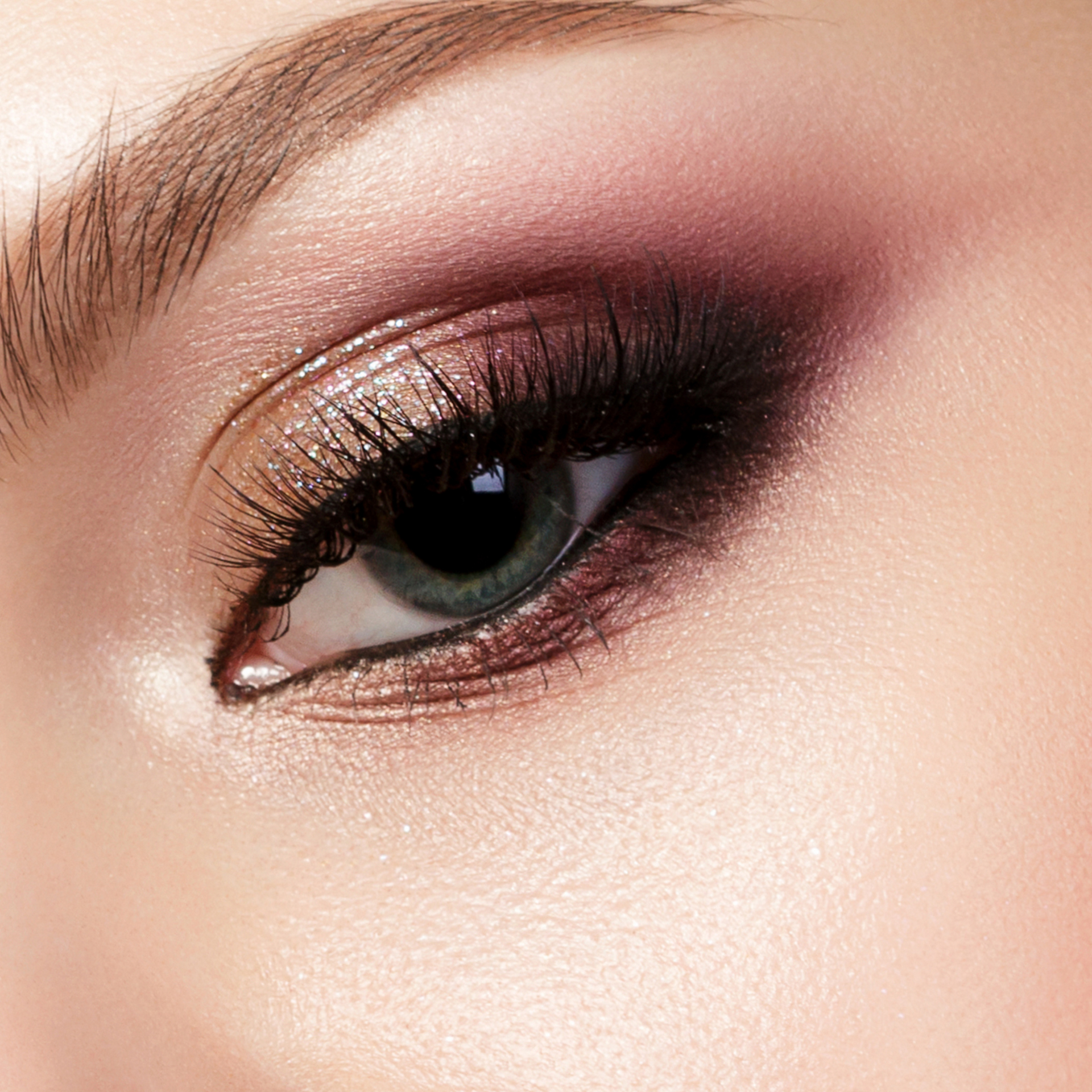 Primer plano de un ojo maquillado con sombra de ojos malva, delineador oscuro y pestañas largas.