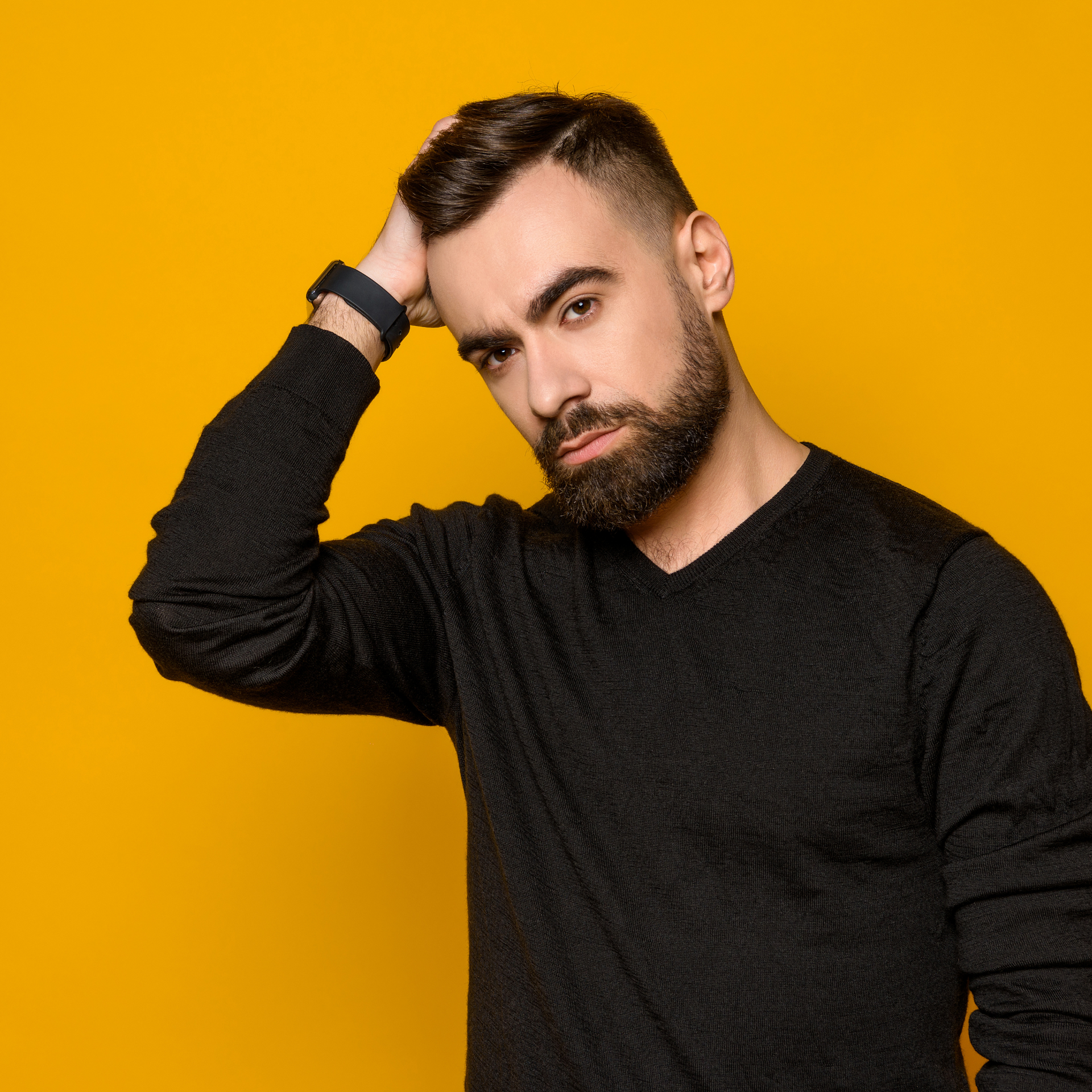 Hombre con suéter negro tocándose el pelo sobre un fondo amarillo brillante