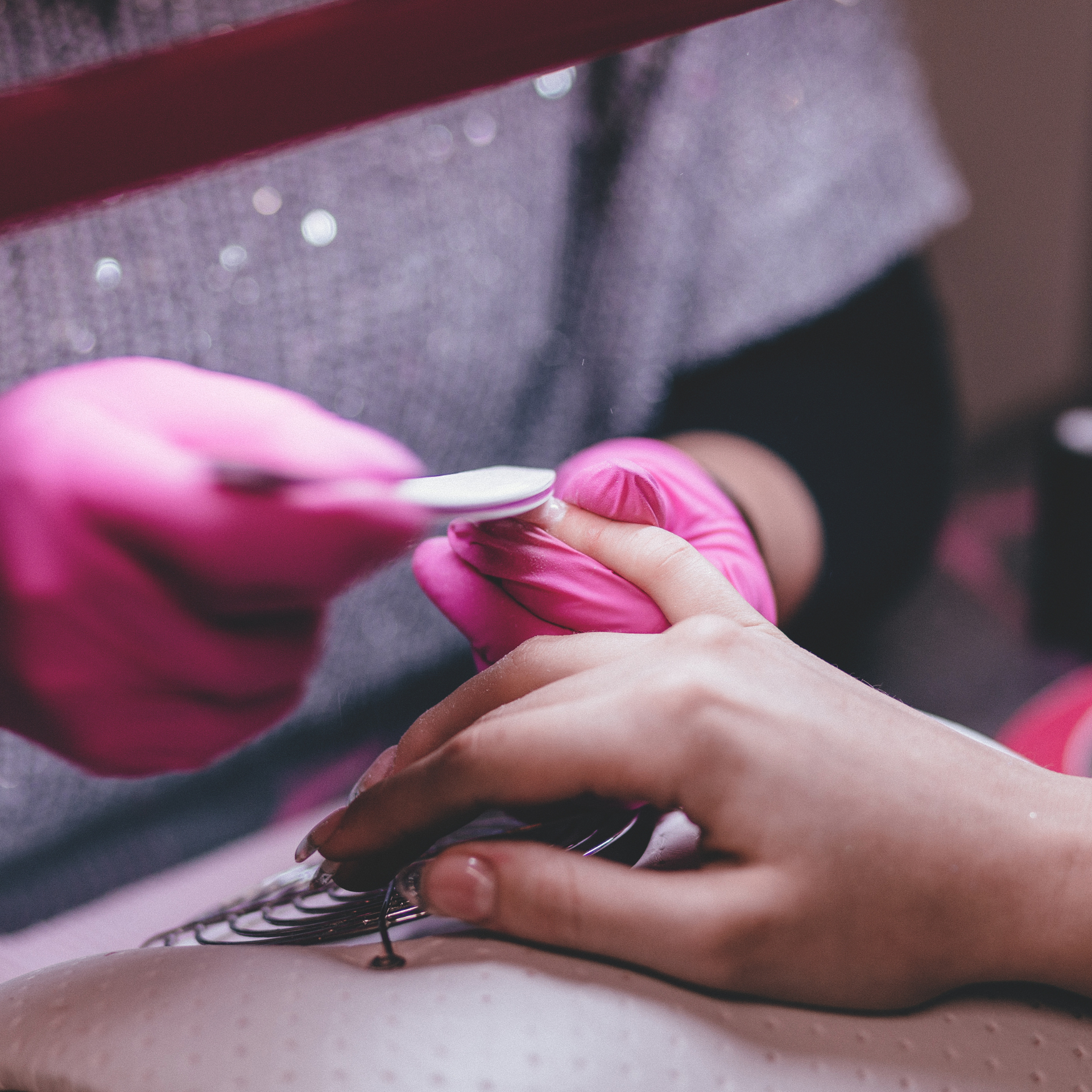 Manos enguantadas limando las uñas de una clienta en un salón de belleza (primer plano)