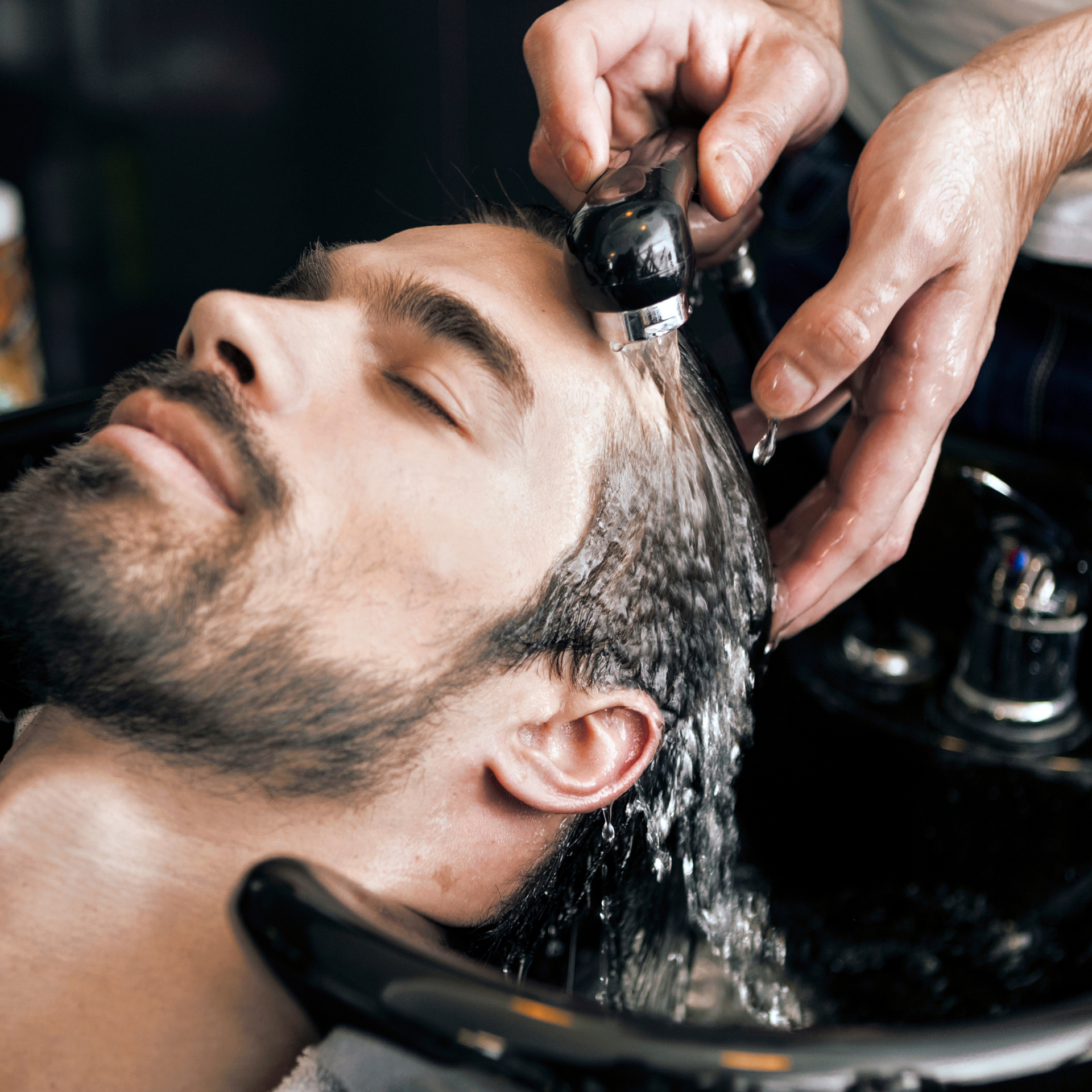 El cabello se está lavando en un lavabo de peluquería con una alcachofa de mano.
