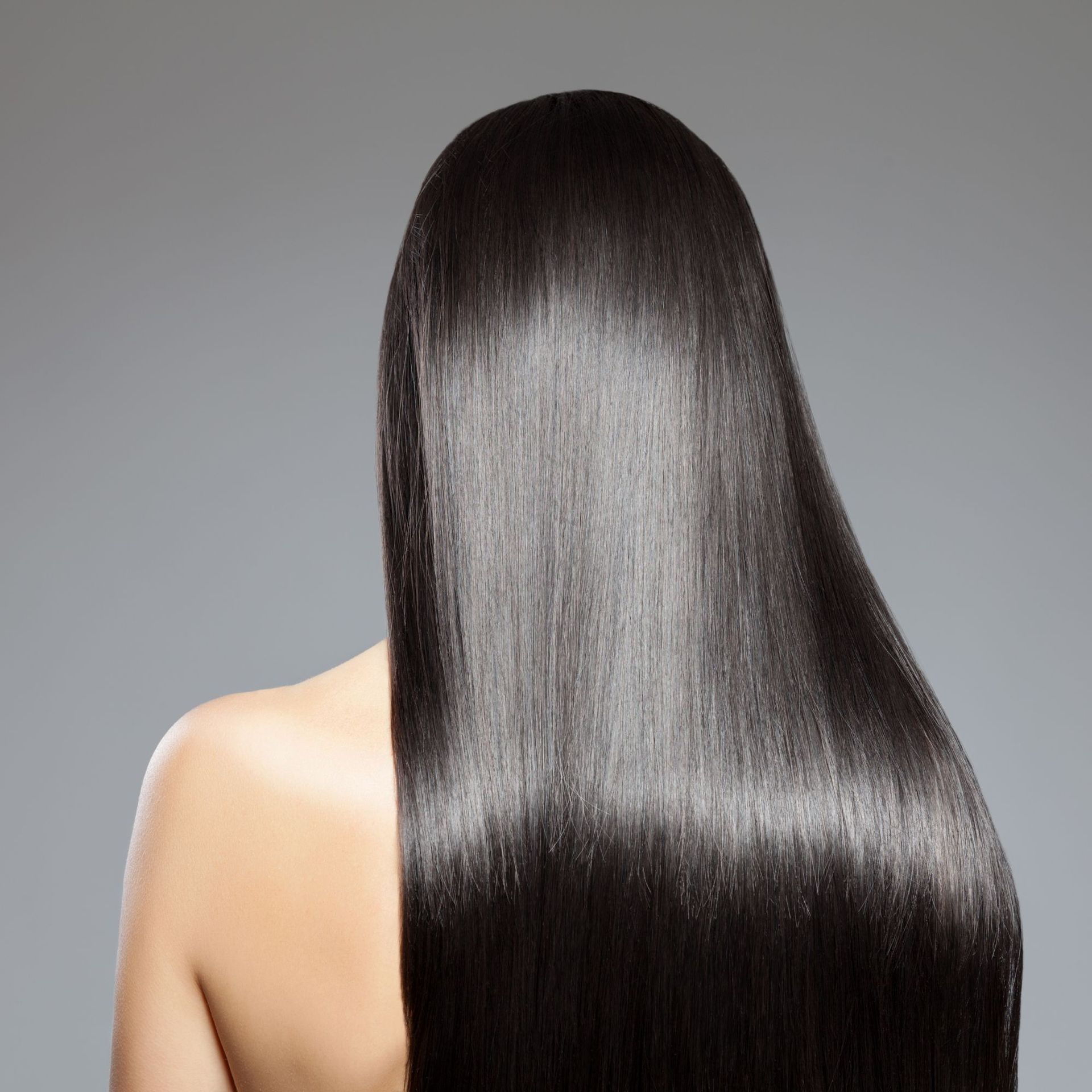 Vista posterior de una persona con cabello largo, liso y negro brillante sobre un fondo gris.