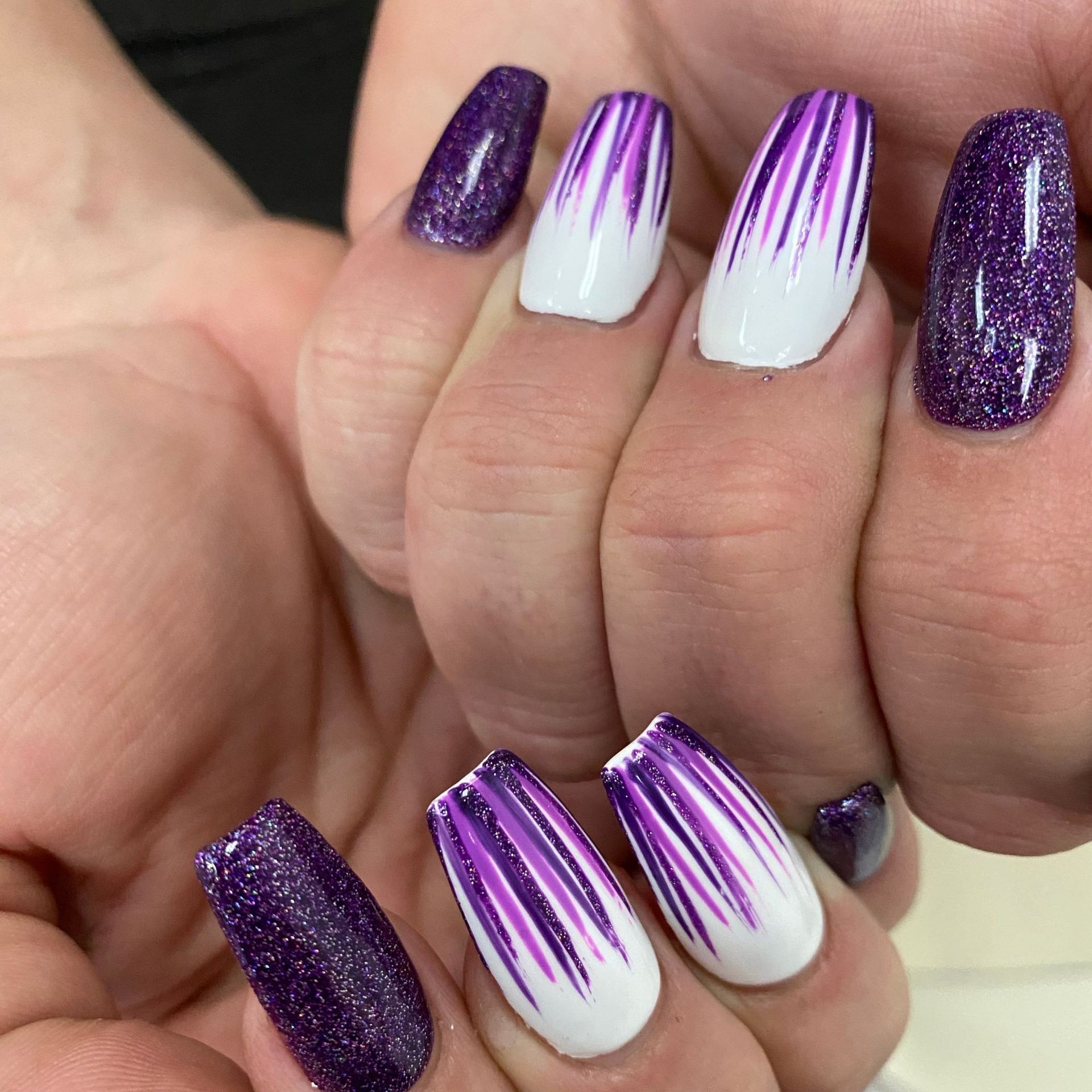 Manos con manicura degradada en blanco y purpurina morada alargada, con detalles de mechones morados.