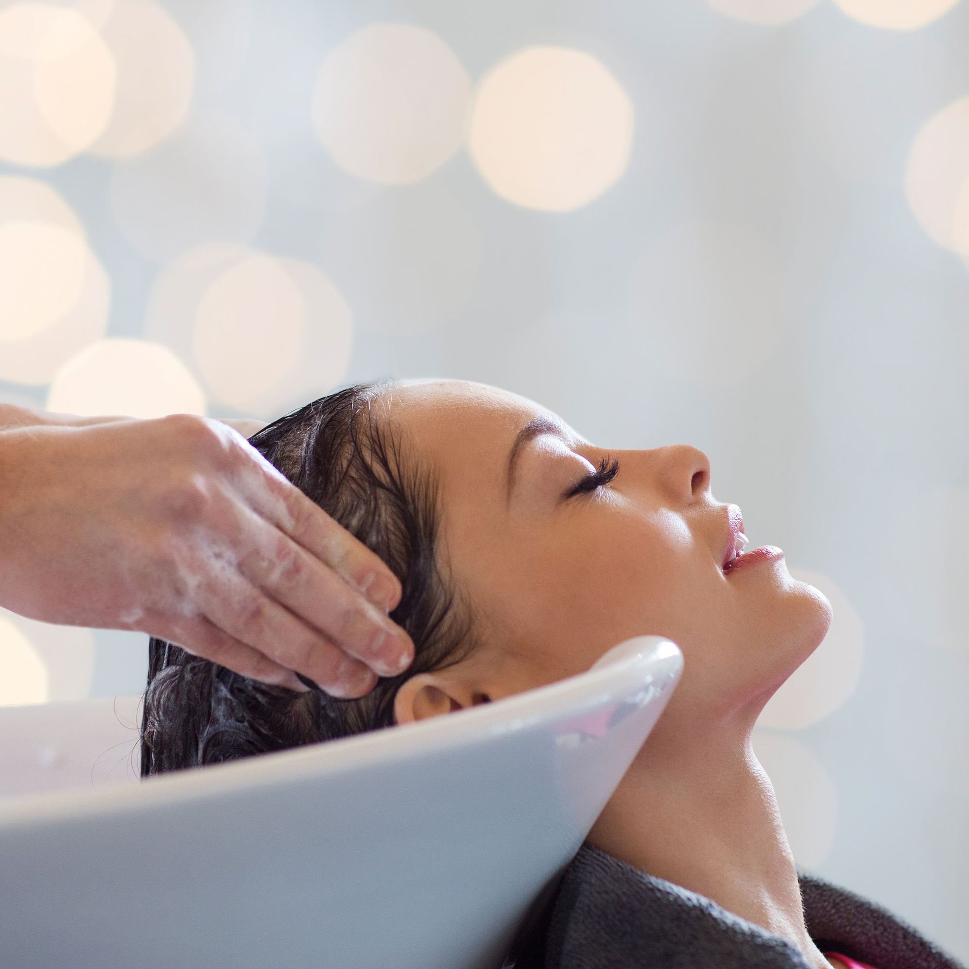 Una clienta recibe un relajante lavado de cabello en el lavabo de la peluquería, con la cabeza inclinada hacia atrás bajo las manos de la estilista.