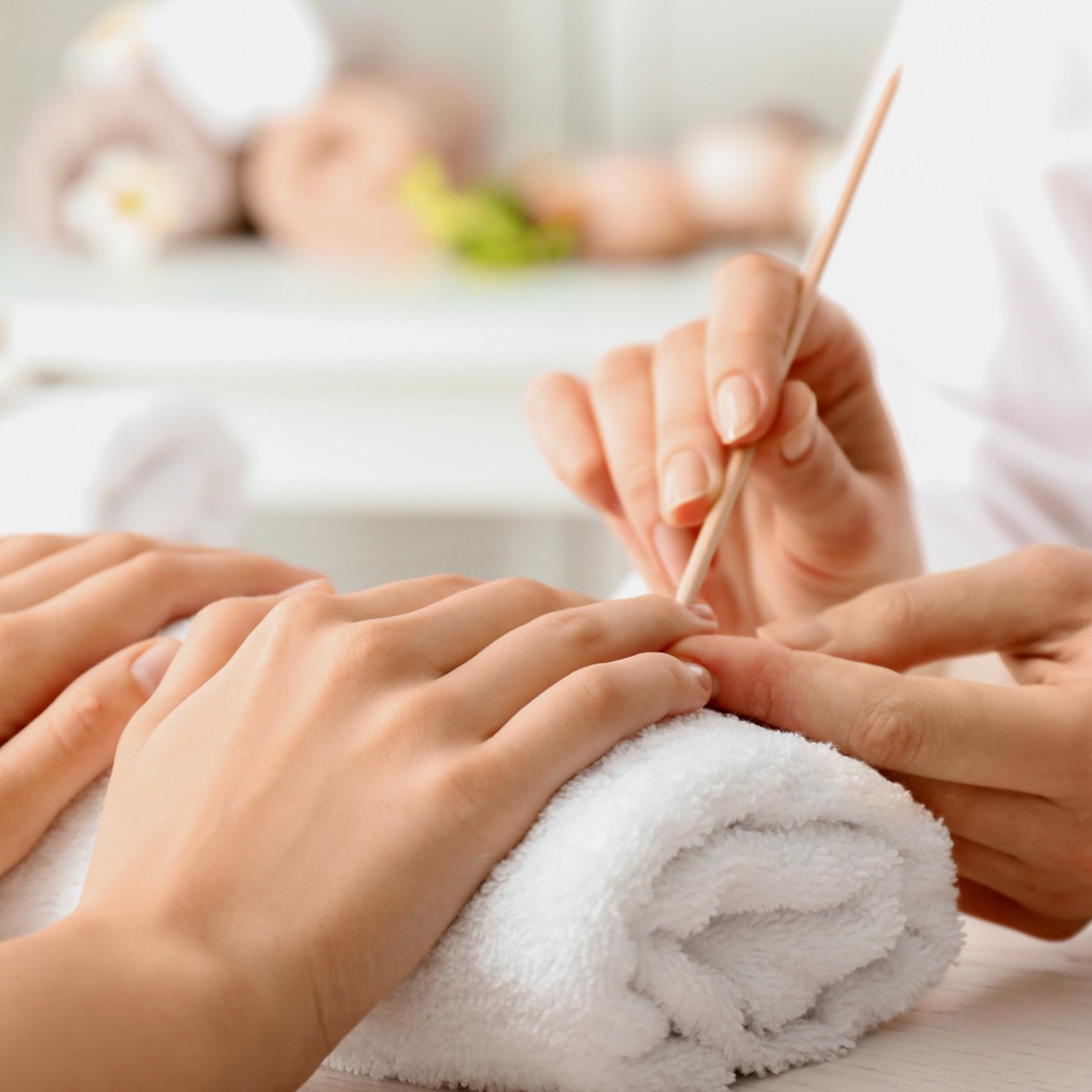 Manos recibiendo una manicura con lima de uñas y toalla blanca en un ambiente de spa con iluminación tenue.