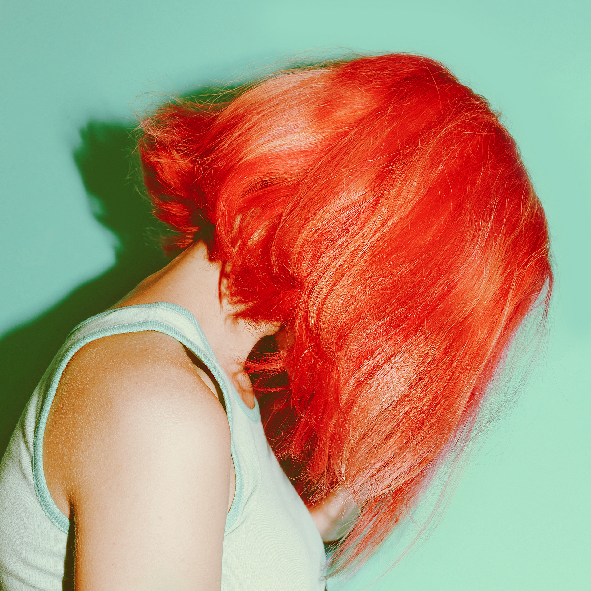 Persona con cabello rojo brillante mirando hacia abajo sobre un fondo verde azulado.