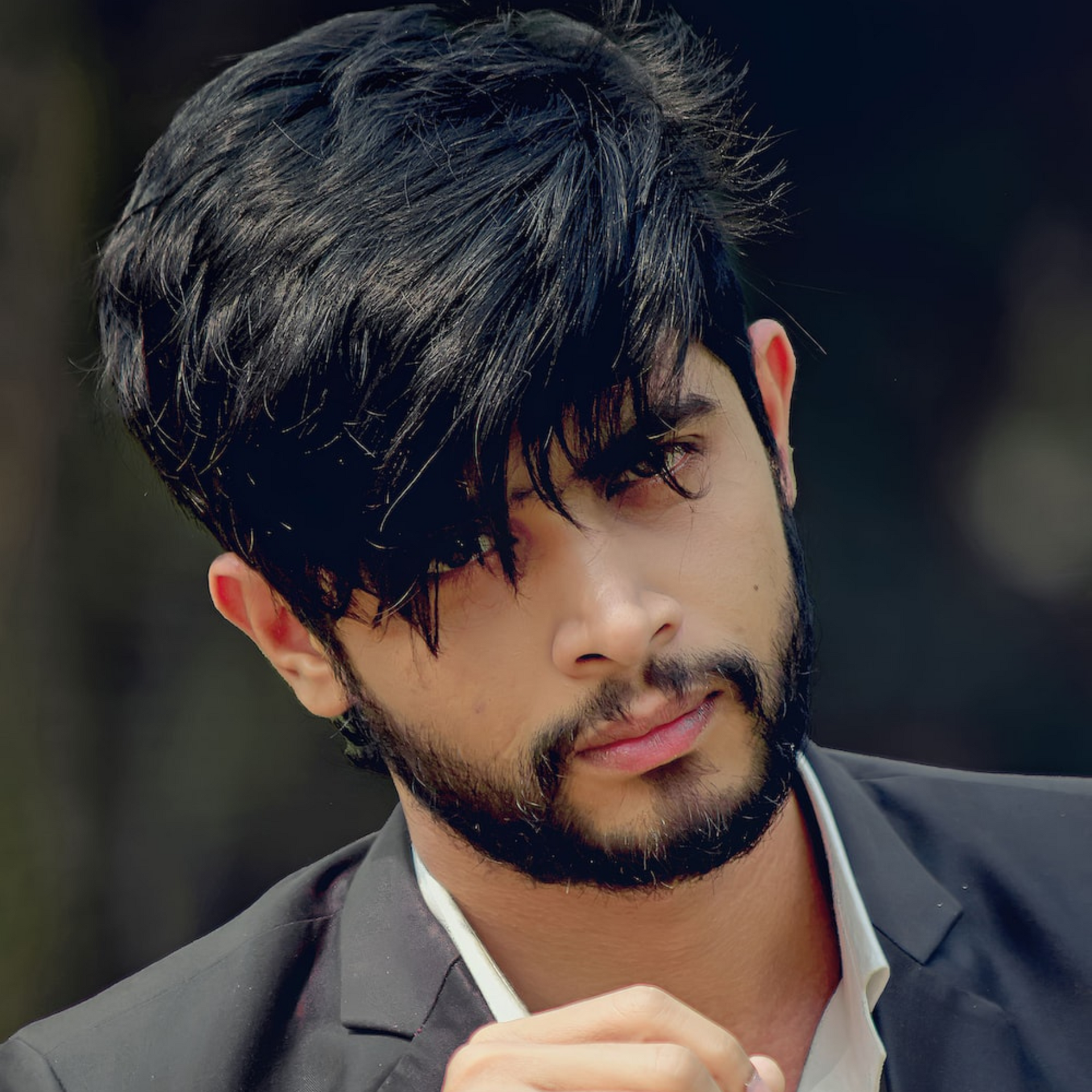 Retrato de un hombre con cabello y barba oscuros, vestido con una chaqueta negra, mirando hacia abajo con expresión serena.