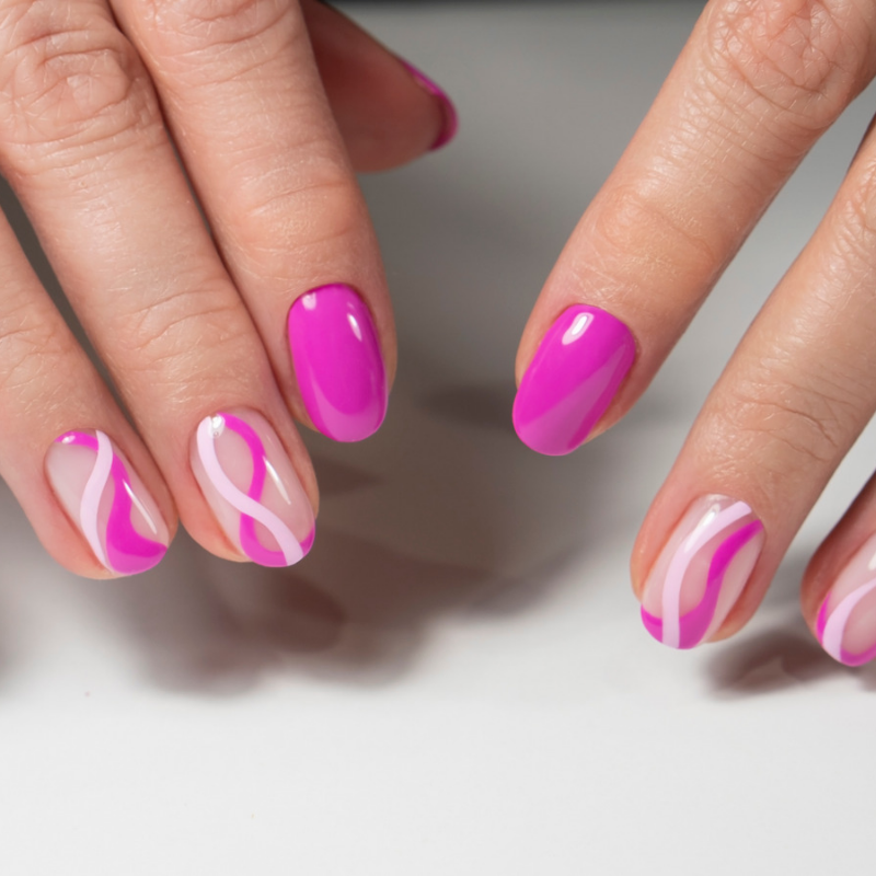 Manos con manicura brillante rosa y blanca con remolinos sobre una superficie blanca.
