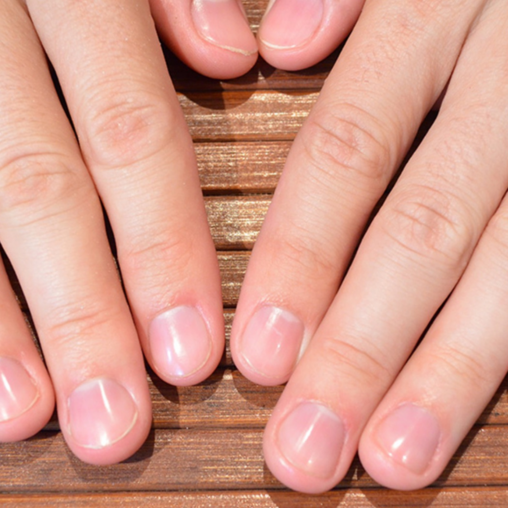 Primer plano de unas manos con uñas naturales cuidadosamente recortadas que descansan sobre una superficie de madera.