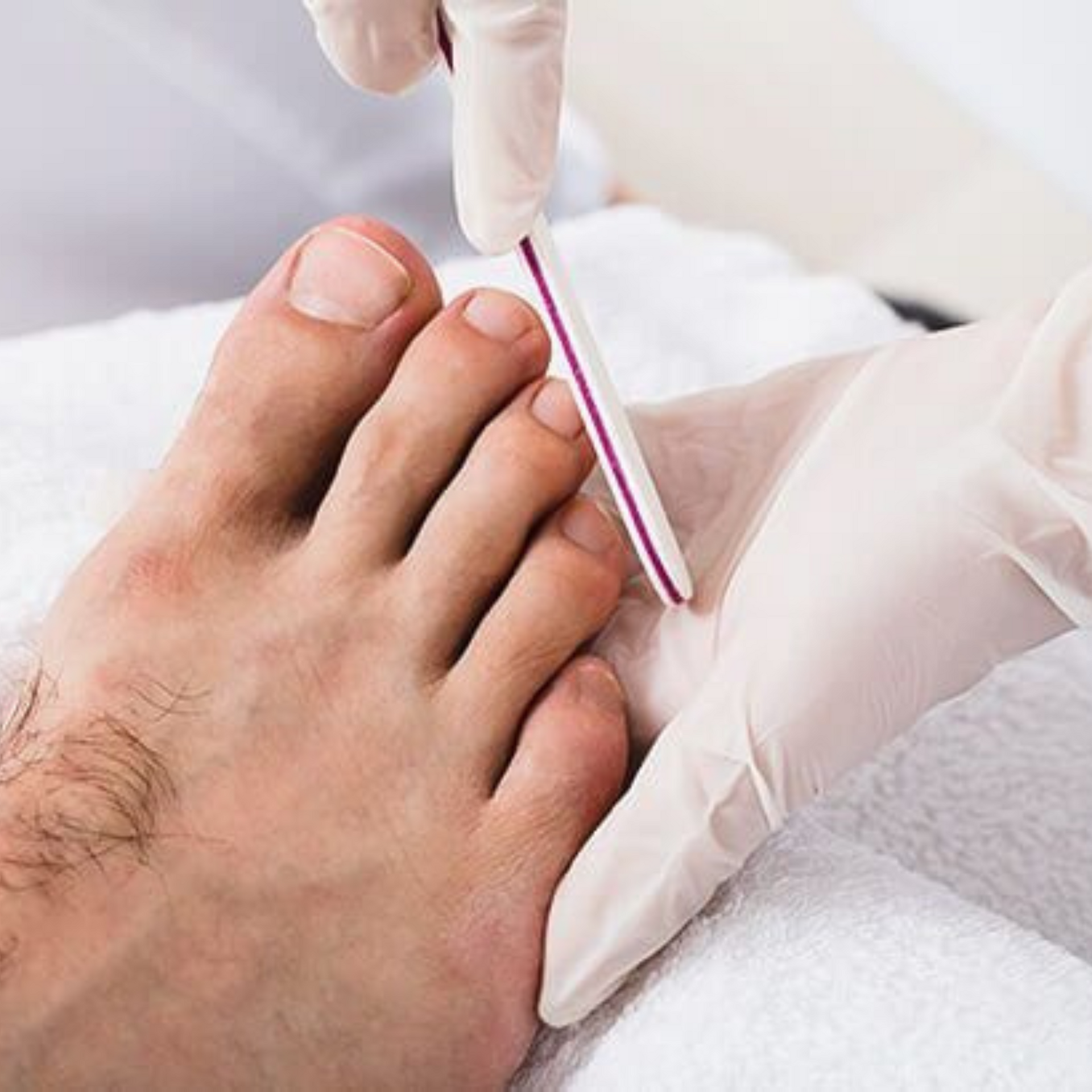 Manos enguantadas limando una uña del pie con una lima de uñas en un entorno clínico.