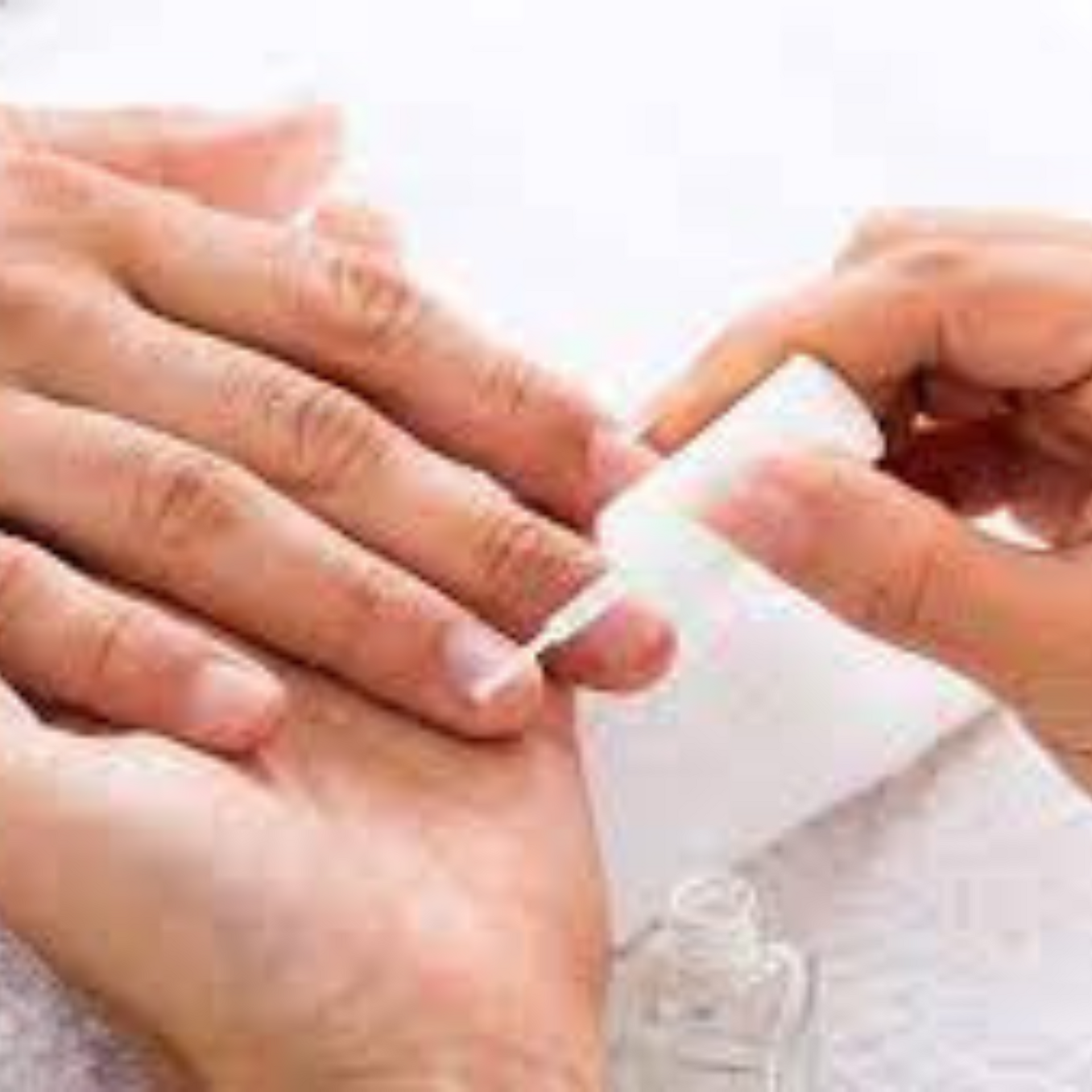 Manos recibiendo una manicura con esmalte de uñas blanco aplicado con un pincel.
