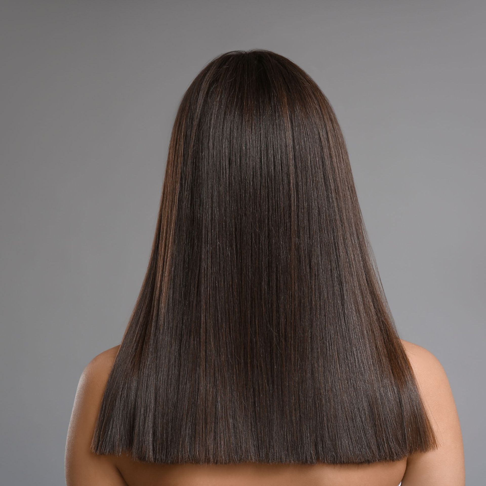 Vista posterior de cabello liso, castaño oscuro, hasta los hombros, sobre un fondo gris.