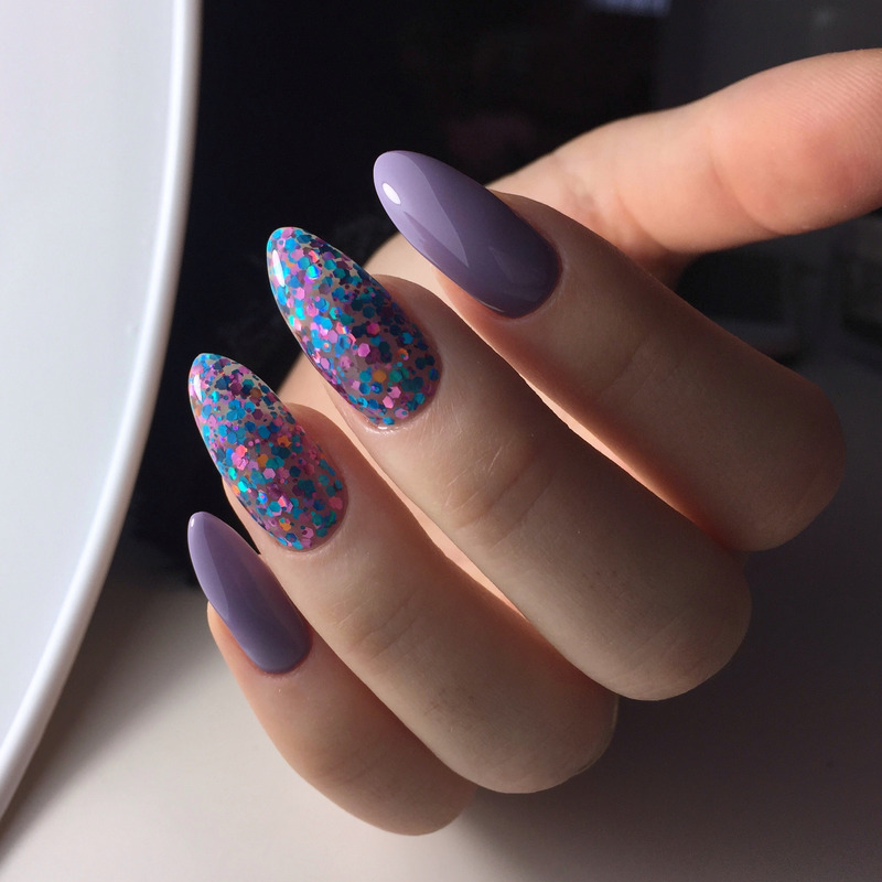 Mano con uñas largas de aguja: diseños en lavanda mate y azul rosado brillante sobre un fondo suave.