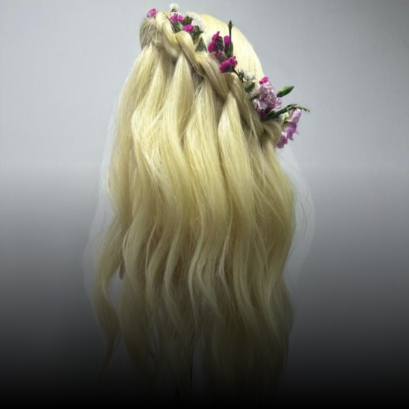 Cabello rubio peinado en una trenza suelta con pequeñas flores moradas entretejidas en ella.