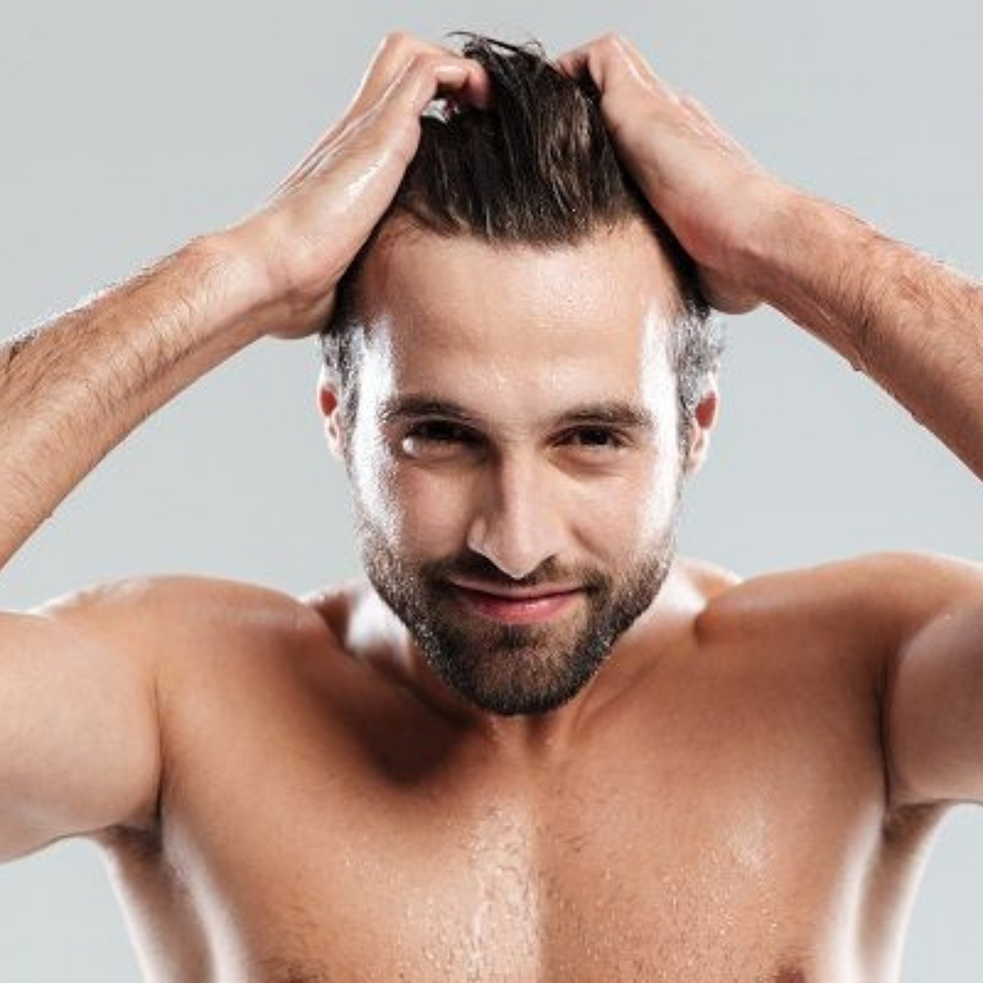 Hombre sin camisa con el pelo mojado, peinándoselo hacia atrás con ambas manos, sonriendo a la cámara.