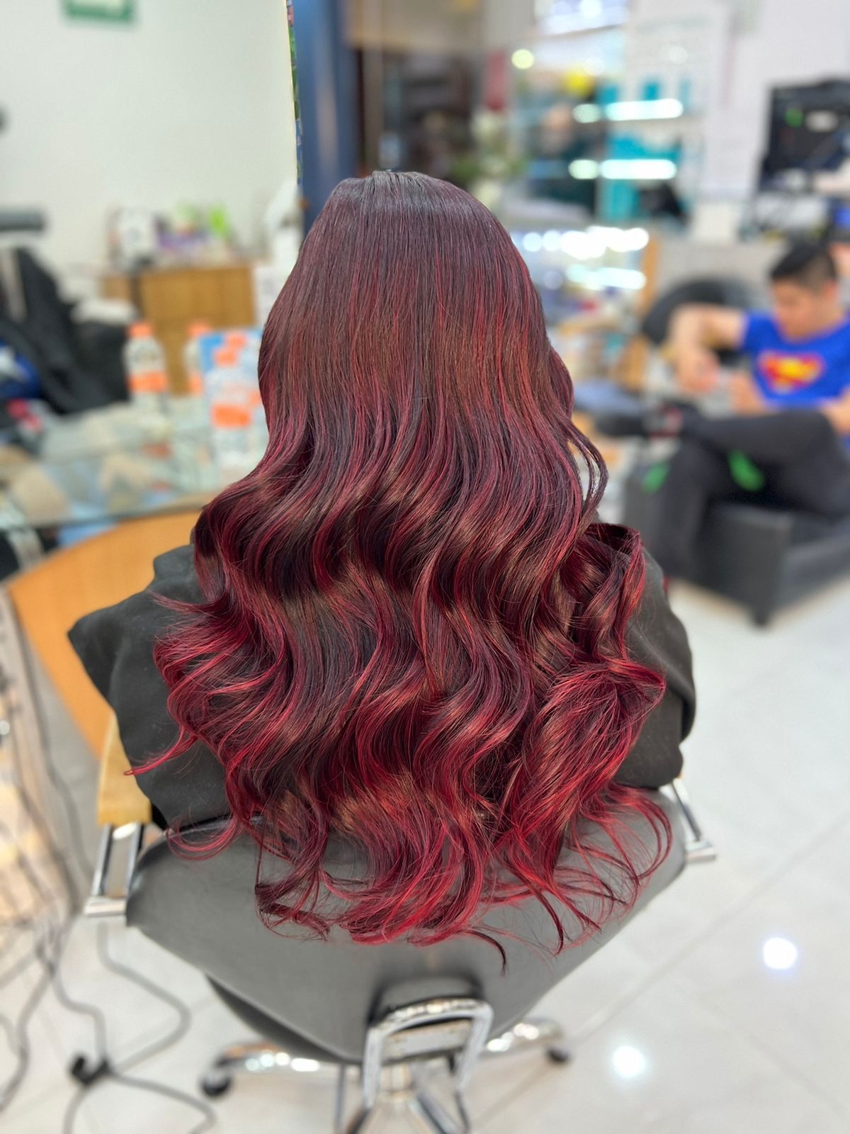 Cabello largo y ondulado color borgoña peinado en una silla de peluquería, con el salón desenfoque de fondo.