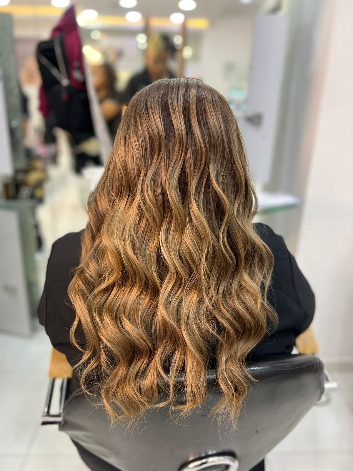 Cabello ondulado castaño claro con reflejos rubios, peinado en capas largas, visto desde atrás en una silla de peluquería.