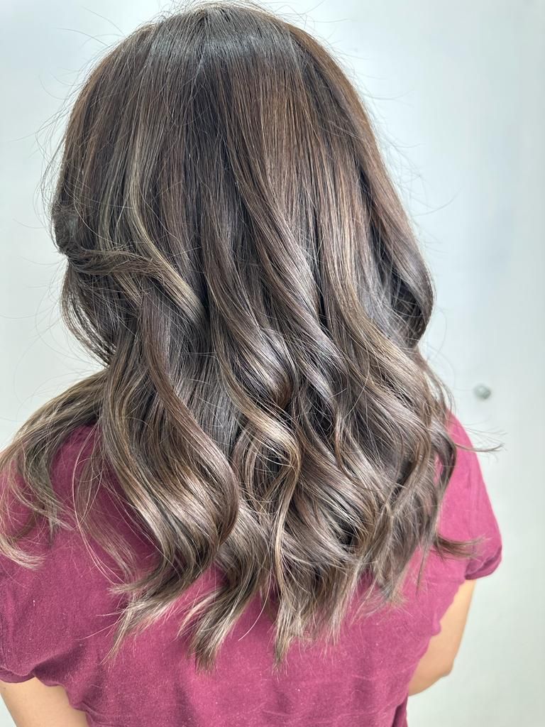Vista trasera de cabello castaño ondulado con reflejos rubios, que termina a la altura de los hombros, sobre una blusa rosa.