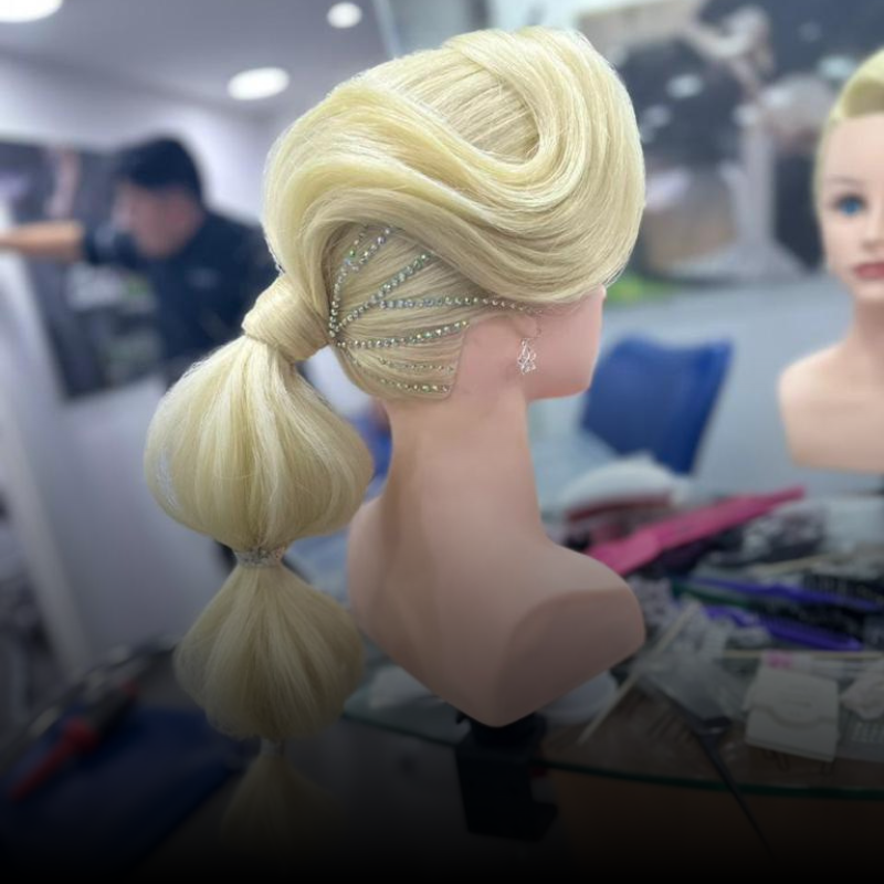 Cabeza de maniquí rubia con peinado recogido y trenza lateral adornada con joyas en un salón de belleza o estudio.