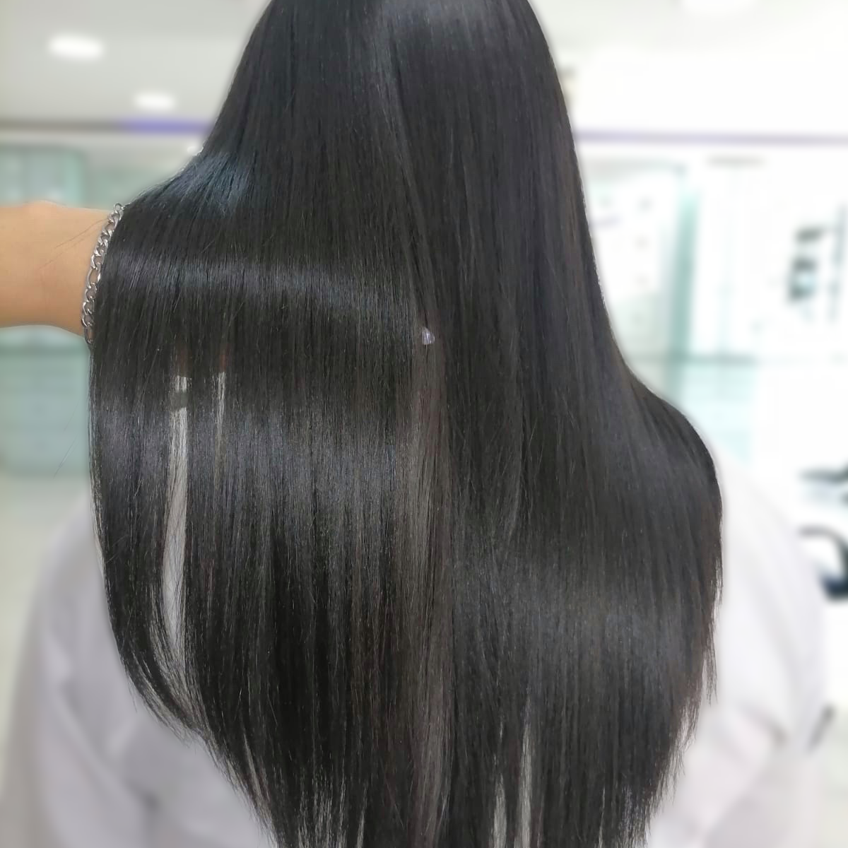 Persona con cabello largo, liso y negro vista de espaldas en un entorno interior luminoso.