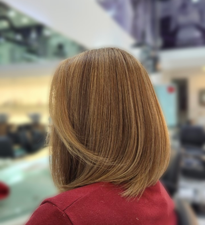 Vista trasera de una persona con cabello castaño rojizo hasta los hombros y una blusa roja dentro de una tienda borrosa.