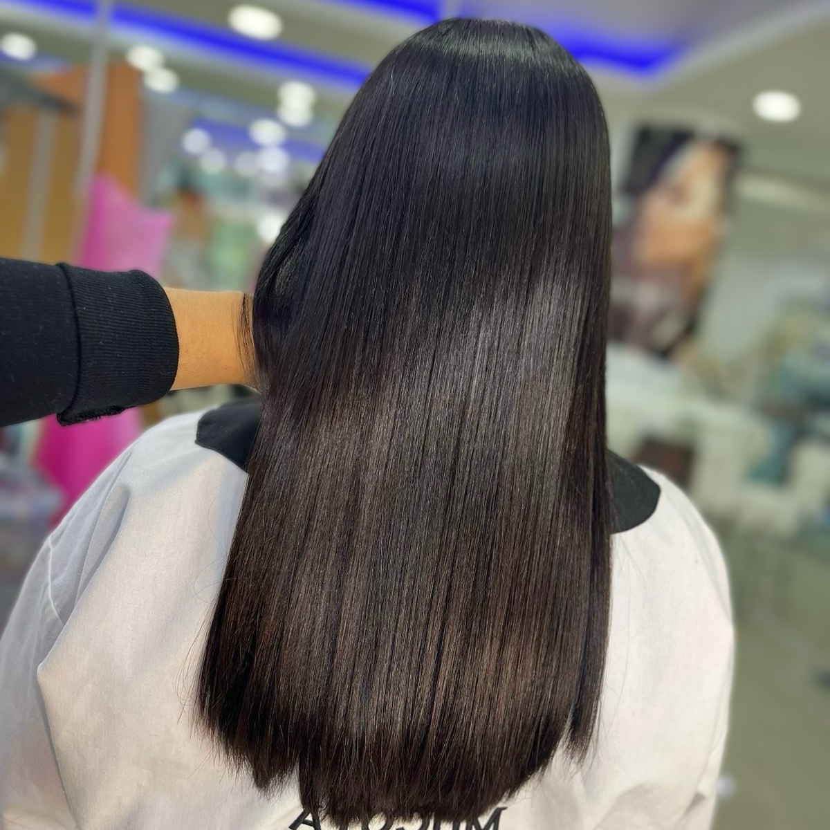 Persona con cabello negro liso hasta los hombros sentada en una peluquería, vista desde atrás.