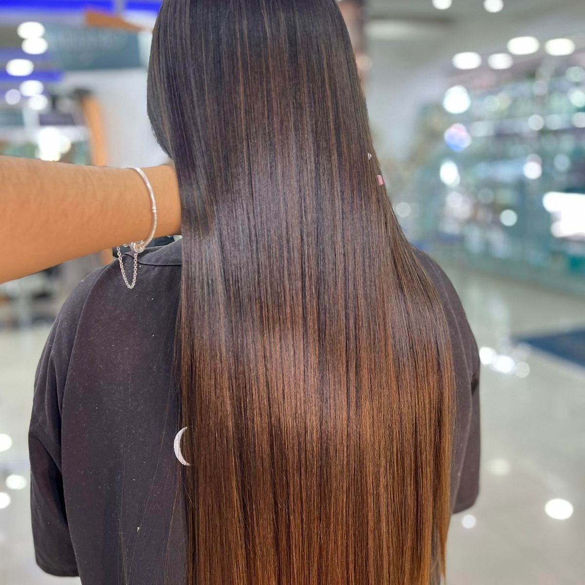 Persona con cabello largo, liso y castaño, siendo sostenida en alto; vista desde atrás en una peluquería.