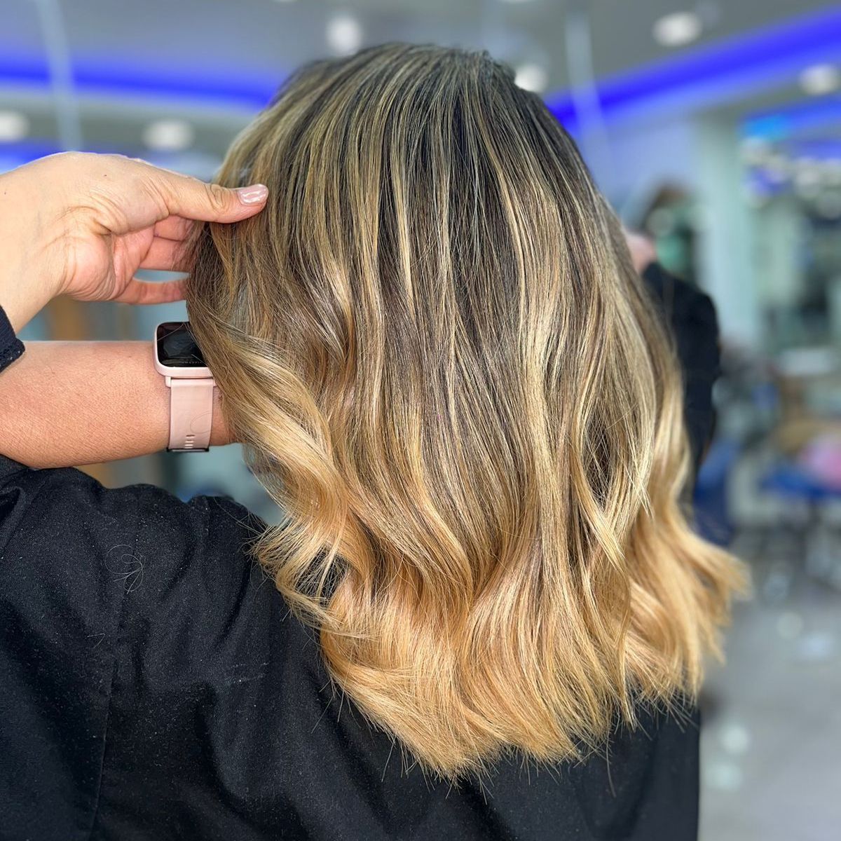 Mano sosteniendo un corte de pelo bob ondulado con mechas rubias en un salón de belleza.