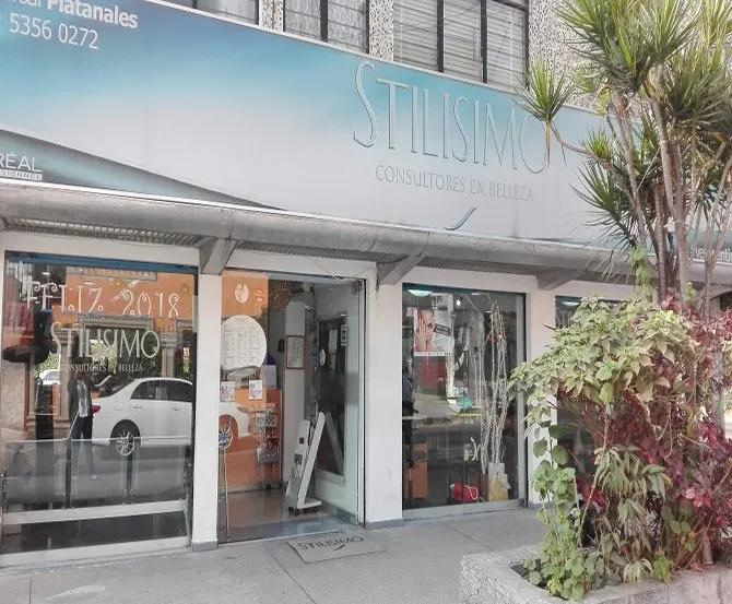 Local comercial con grandes ventanales, un toldo blanco y una palmera en maceta en el exterior, situado en una acera de la ciudad.