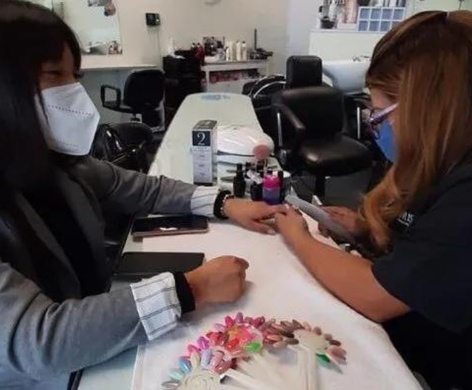 Dos personas enmascaradas se hacen la manicura en una mesa de un salón de uñas.