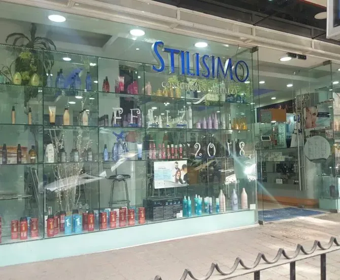 Escaparate de la tienda con productos para el cabello y artículos de peluquería, con el letrero “STILISMO” sobre la entrada.
